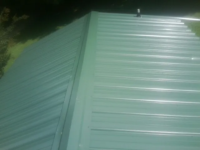 New green metal panels meeting at the ridge of a roof — Flat Roof Repair work by our crew in Greensboro