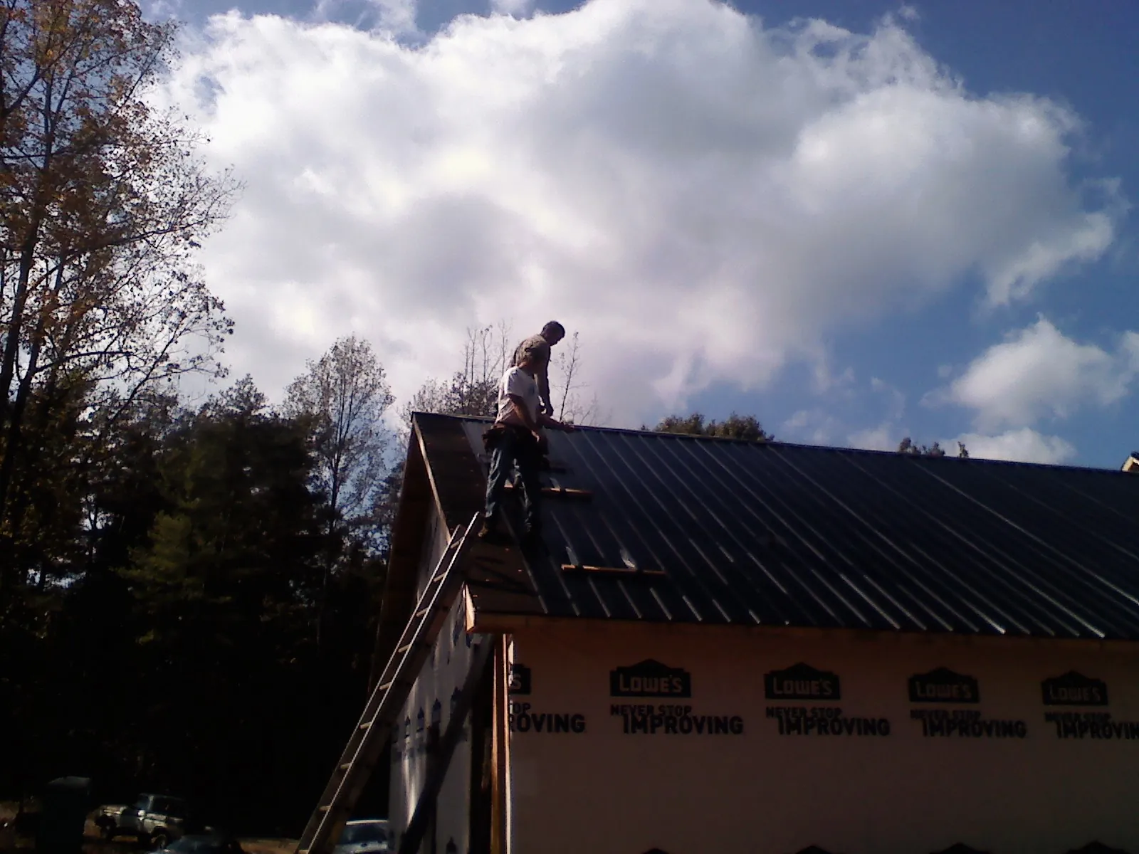 Roofer fastening dark metal panels high against a cloudy sky, from a Roof Inspection job in Greensboro